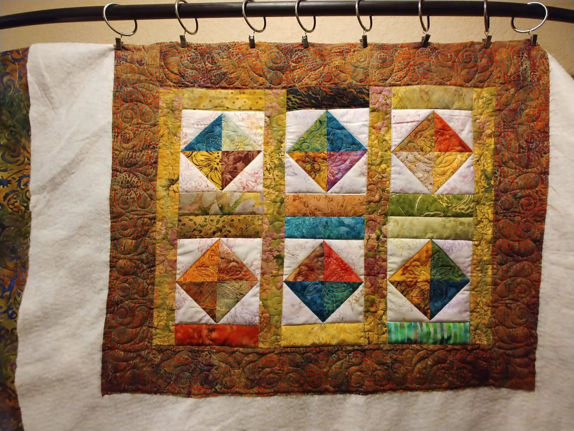 A quilt hanging on the wall with hooks.