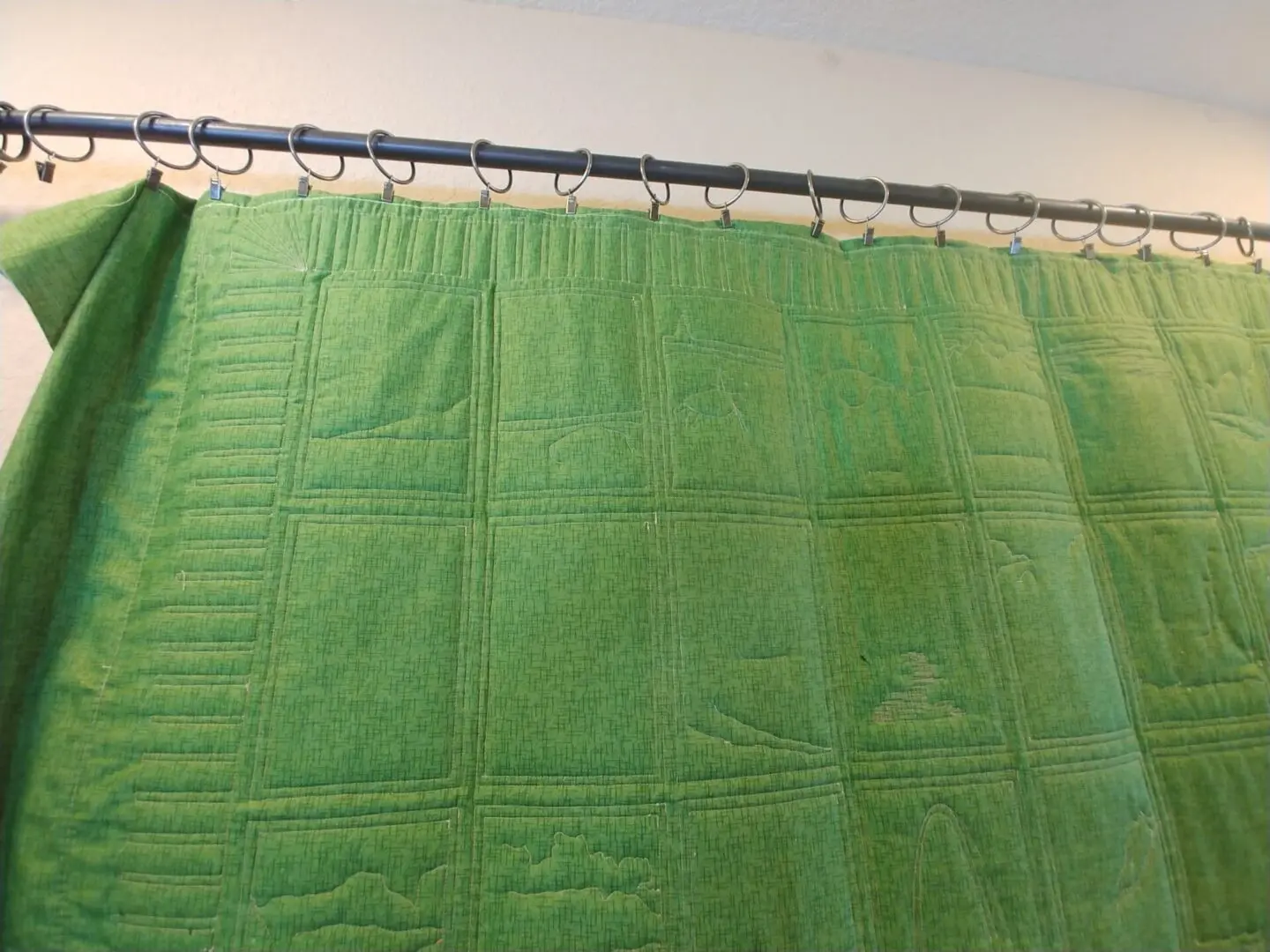 A green quilt hanging on the side of a shower curtain.