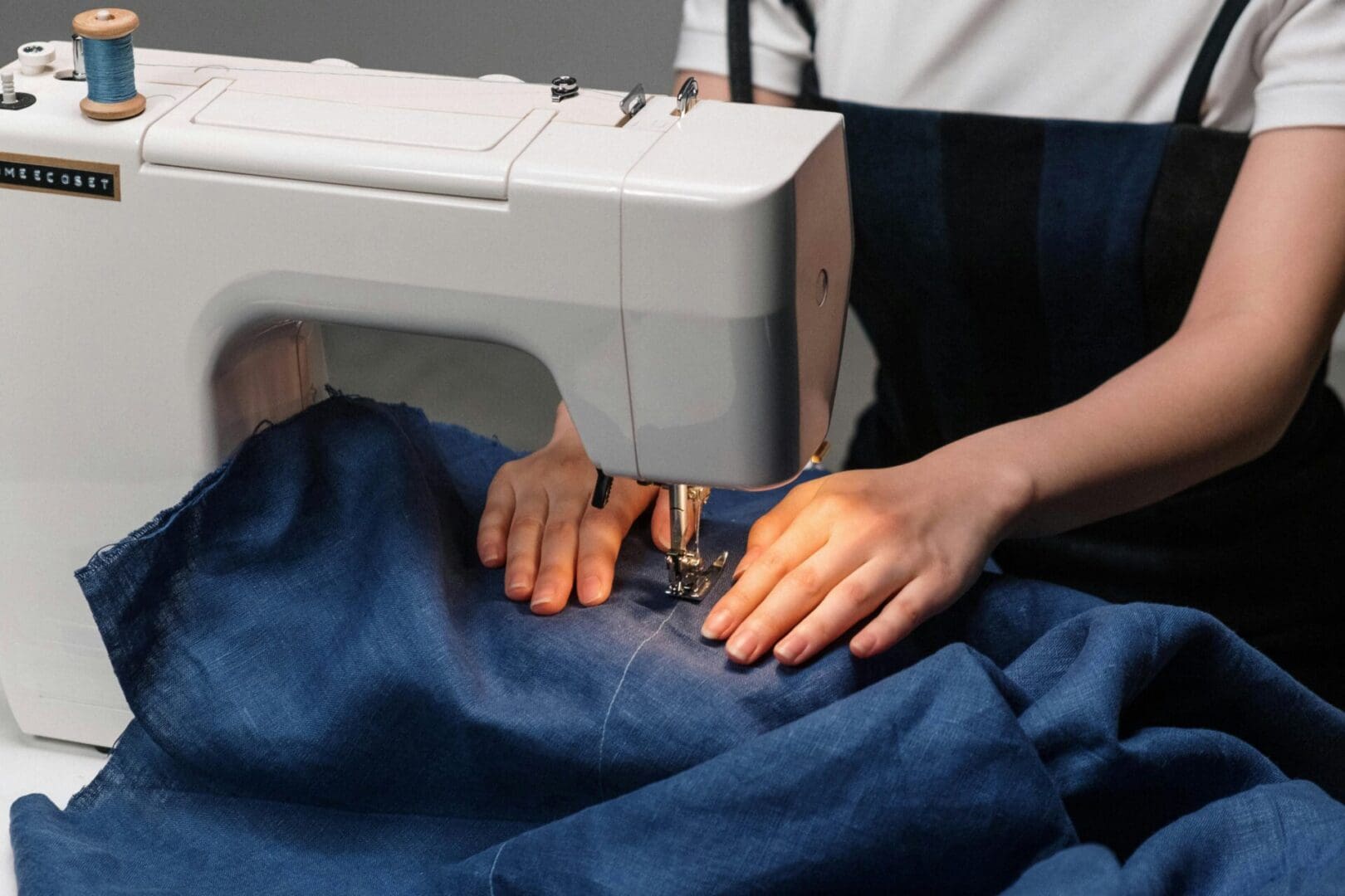 A person using an electric sewing machine on a blue cloth.