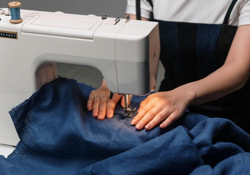 A person using an electric sewing machine on a blue cloth.